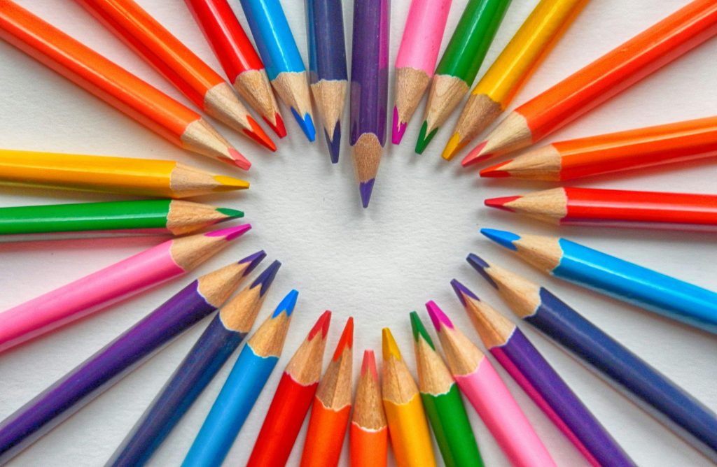 An array of color as colored pencils lay arranged in a flat display of a heart shape.