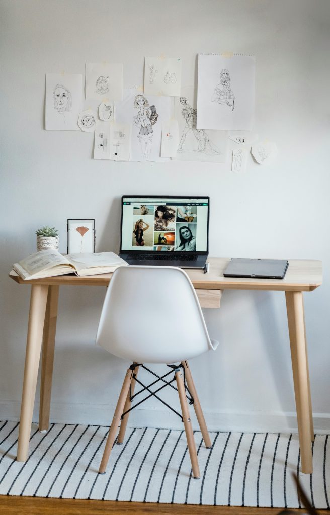 The inside of an artist's studio, with their artwork on the wall and reference photos on their desktop computer.